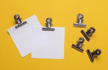 Memo white square sheets of paper with binder clips on yellow background. Stationery, education,...