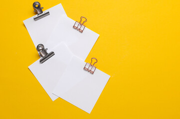 Memo white square sheets of paper with binder clips on yellow background. Stationery, education,...