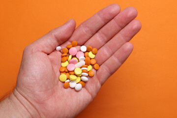 Many different pills in a man's hand on an orange background