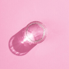 Glass of water with a reflection and shadow on a pink background. Minimalism. top view