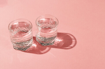 Glasses of water with reflection and shadow on pink background. Minimalism.