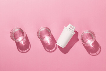 Cartridge filter for filtering water and glasses of clean water on pink background with shadow....