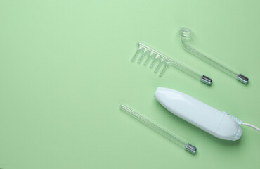 Acne treatment. Device for local darsonvalization with nozzles on green background. Beauty concept. Flat lay. Copy space