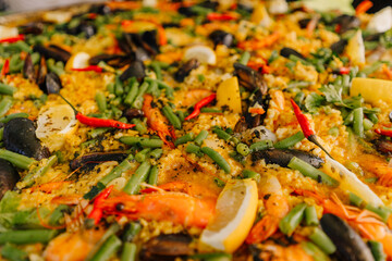 Close-up of a vibrant seafood paella featuring shrimp, mussels, green beans, lemon, rice, and red chili. Rich texture and colorful ingredients..