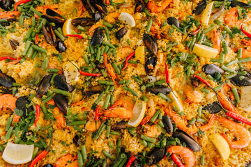Colorful seafood paella with mussels, shrimp, green beans, red chili, rice, and lemon wedges. Close-up top view with rich texture and detail..