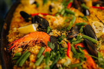 Close-up of colorful seafood paella with shrimp, mussels, lemon wedges, green beans, and herbs. Rich in texture and vibrant in color..