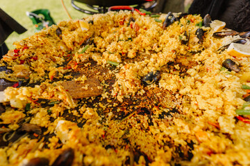 Nearly empty paella pan showing the crispy rice bottom and scattered seafood remains after a large outdoor meal, with a wooden spatula resting in the pan..
