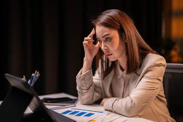A woman is sitting at a desk with a laptop and a stack of papers