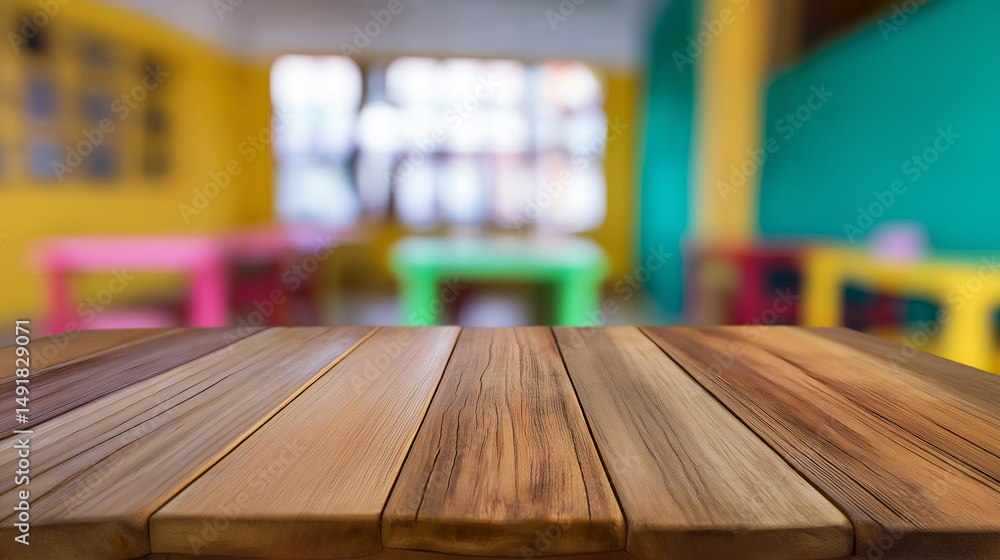 Poster empty wooden desk in a colorful classroom with blurred desks and windows in the background.