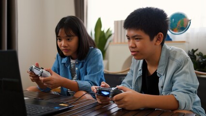 Asian teenage boy and girl playing video games at home together. Concept of digital lifestyle, esports, fun learning, teamwork, and modern entertainment for kids and teens indoors.