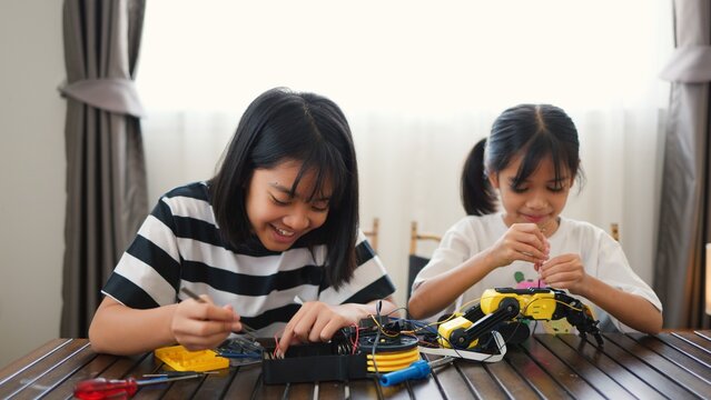 Two Asian girls working together on robotics project at home. Promoting STEM education, teamwork, coding, and problem-solving through hands-on engineering and creative learning.