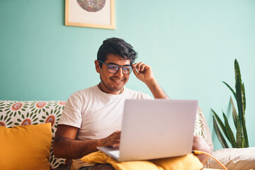 Hombre joven reacciona con alegría durante videollamada desde casa. Expresa emoción y conexión humana en contexto de teletrabajo. Perfecta para representar logros o buenas noticias laborales. - obrazy, fototapety, plakaty
