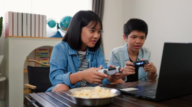 Asian teenage boy and girl playing video games at home together. Concept of digital lifestyle, esports, fun learning, teamwork, and modern entertainment for kids and teens indoors.