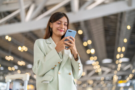 Confident traveler using smartphone at airport terminal, businesswoman smiling while checking flight updates, lifestyle modern working woman travel planning executive checking phone before boarding