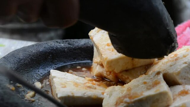 Preparing tofu or tahu on stone mortar and pestle with ingredient