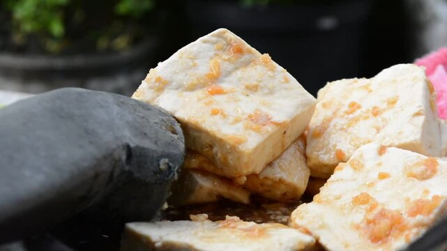 Preparing tofu or tahu on stone mortar and pestle with ingredient