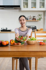 Fit woman enjoys healthy fresh vegetables and fruits breakfast sitting in the kitchen.