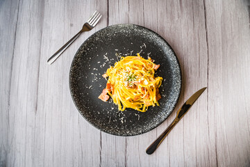 Carbonara with ham cream and cheese served on a black plate