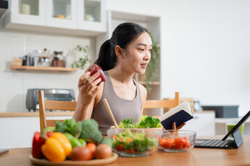 Fit woman enjoys healthy fresh vegetables and fruits breakfast sitting in the kitchen.