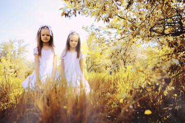 A pair of twin girls are walking in the autumn garden. Children walk in the park.