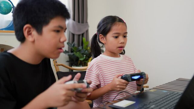 Asian teenage boy and girl playing video games at home together. Concept of digital lifestyle, esports, fun learning, teamwork, and modern entertainment for kids and teens indoors.