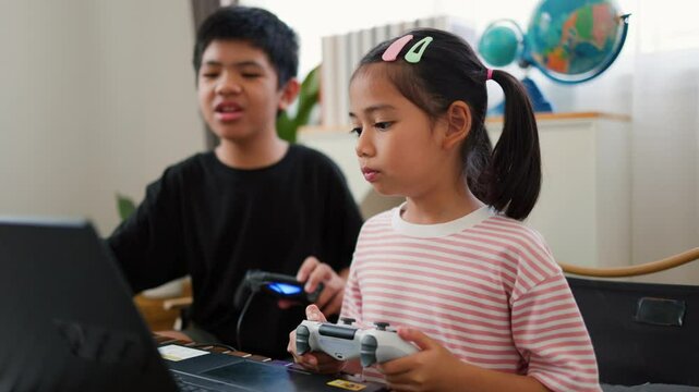 Asian teenage boy and girl playing video games at home together. Concept of digital lifestyle, esports, fun learning, teamwork, and modern entertainment for kids and teens indoors.