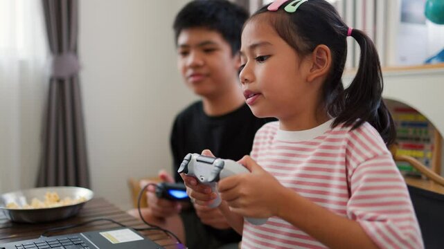 Asian teenage boy and girl playing video games at home together. Concept of digital lifestyle, esports, fun learning, teamwork, and modern entertainment for kids and teens indoors.