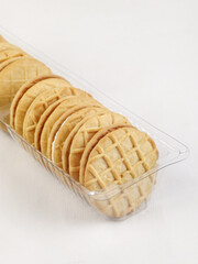 Close-up image of round butter cookies arranged in a transparent plastic tray against a white background.