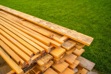 Fototapeta premium Wooden construction boards close-up stacked near green lawn grass
