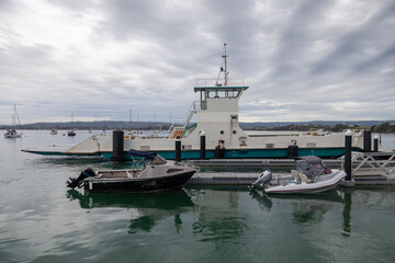 The Matakana Ferry sits docked in tranquil waters, alongside smaller boats, under a cloudy sky. The ferry provides transport for locals and tourists. Omokoroa, Bay Of Plenty, New Zealand