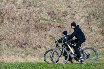Fototapeta premium Two people biking together on a grassy hill, enjoying a sunny day outdoors.