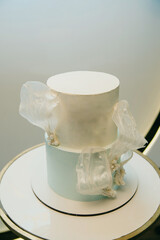 white and blue two-tier cake with decorative inserts stands on a round table on an isolated...