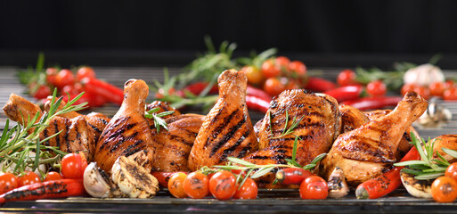 Grilled chicken legs, drumsticks and thighs on the hot flaming barbecue grill with smoke on dark background..