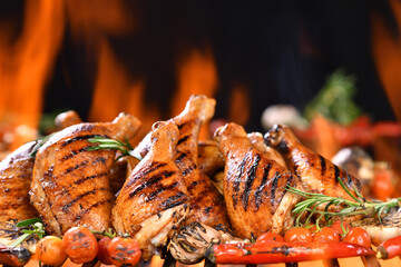 Grilled chicken legs, drumsticks and thighs on the hot flaming barbecue grill with smoke on dark...