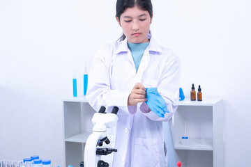 Fototapeta premium Asian female scientist preparing for an experiment, wearing laboratory gloves in a modern lab. Science, laboratory, scientist, gloves, and research are depicted with a professional atmosphere.