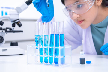 Teen scientist girl conducting science test by carefully evaluating blue solution in laboratory....
