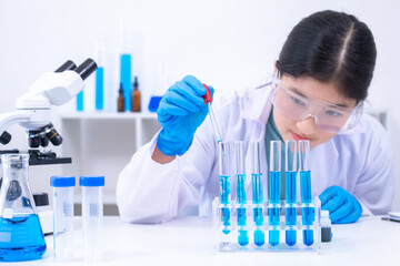 Teen scientist girl conducting science test by carefully evaluating blue solution in laboratory....