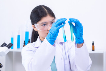A teenage girl scientist in a laboratory carefully inspects liquid sample in pipette while wearing...