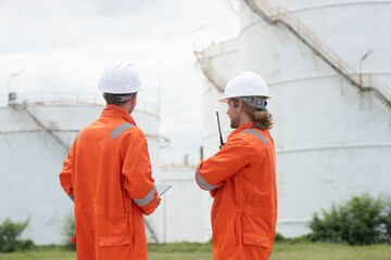 Worker in safety gear using tablet near industrial storage oil tanks refining petrochemical...