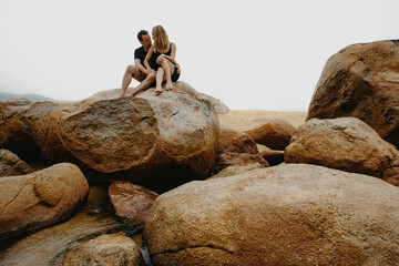 Young caucasian couple relaxing on large boulders by the beach