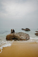 Female and male adults relaxing on rocky beachfront with ocean view