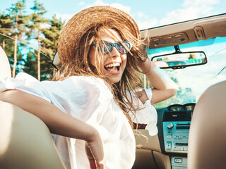 Portrait of young beautiful and smiling hipster female in convertible car. Sexy carefree woman...