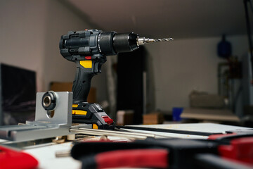 Electric cordless drill with bits and hand tools on workbench in workshop. Home renovation, construction and repair concept