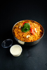A vibrant bowl of biryani topped with herbs and served with tangy raita, ready to enjoy