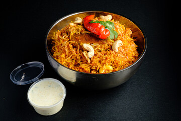 A colorful bowl of biryani, rich in spices, garnished with cashews and herbs, plus tangy sauce
