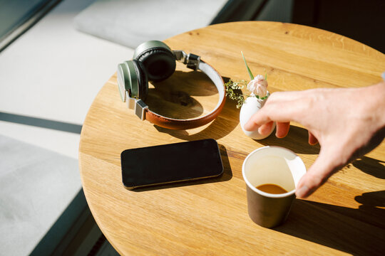 Hand reaching for coffee cup on a wooden table with headphones and smartphone in a caf�