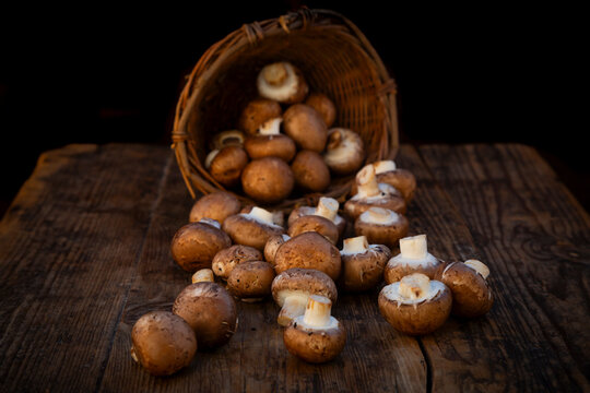 Brown Agaricus bisporus mushrooms spilling from a willow basket onto a wooden table