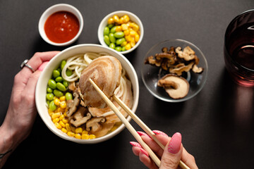 Noodles are being lifted with chopsticks from a flavorful bowl filled with fresh ingredients