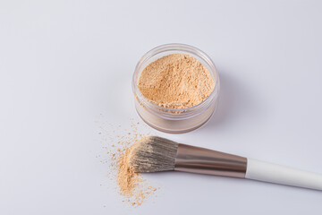 An open glass jar with dry powder and a professional makeup brush on a white background. A copy...