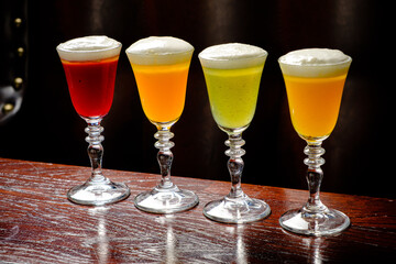 Colorful cocktails with frothy tops are elegantly displayed on a wooden bar in a dimly lit lounge